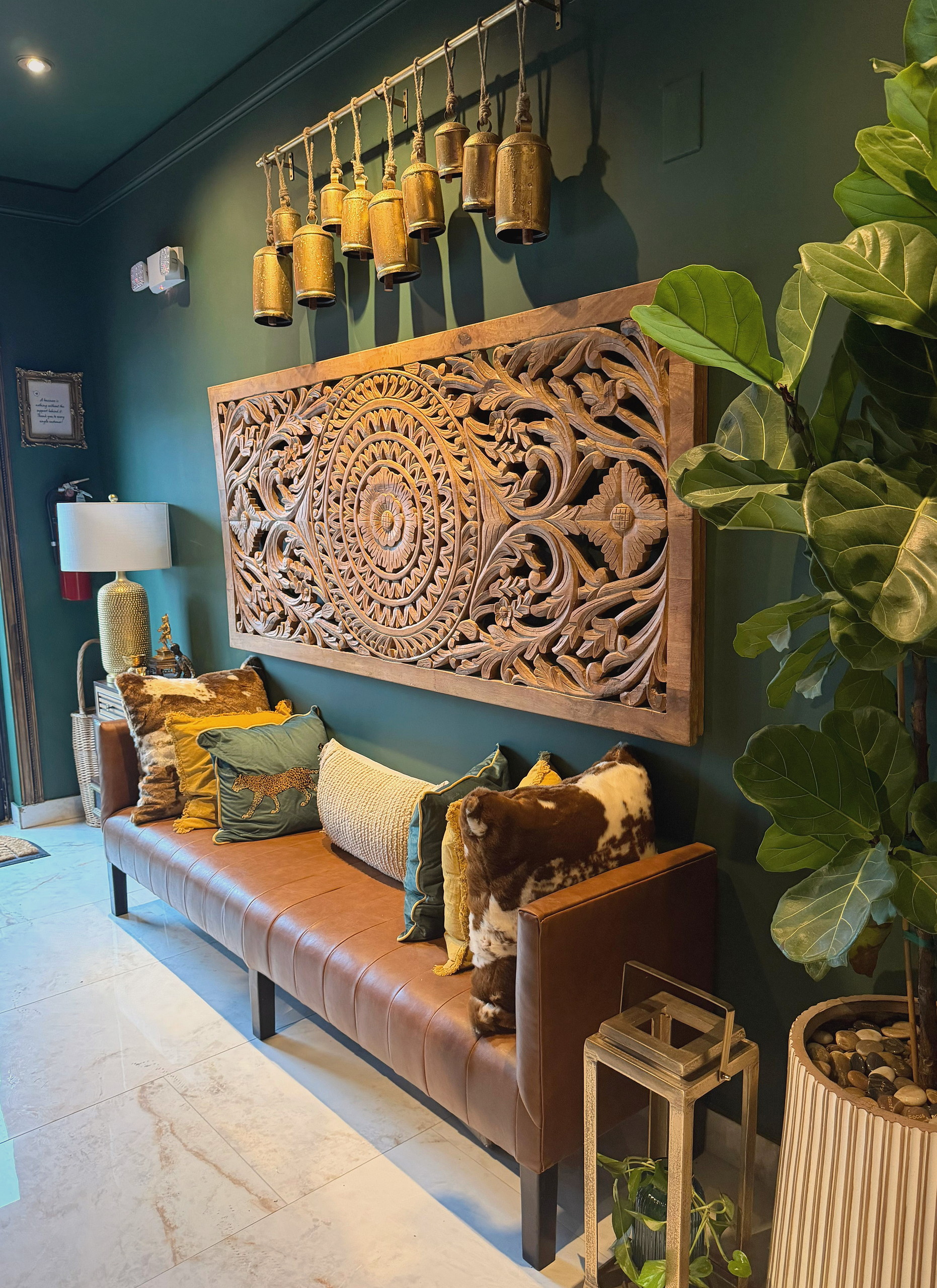Waiting bench in cognac leather beneath a carved wooden panel and brass bells